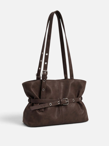 Close-up of the buckle and metal eyelet belt detail on the front of the tote bag